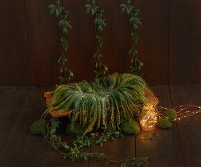 Cot for photo shoots of a newborn with green wool, moss and green leaves. Fantasy lights in the jar. Shoot set up with prop bed and wood backdrop. 