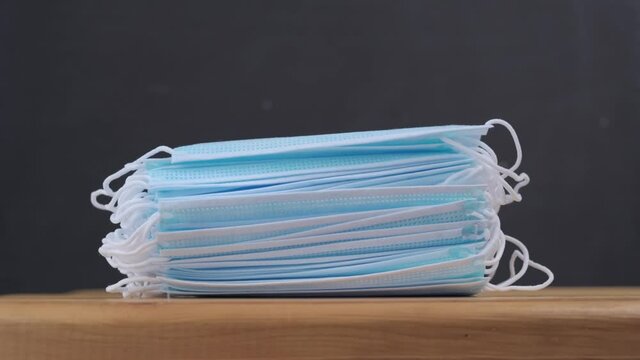 from a stack of new clean medical masks that lie on a wooden table, one by one is taken one at a time to protect against coronavirus