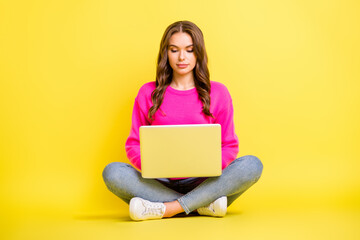 Full size photo of young serious focused girl sit floor with crossed legs working in laptop isolated on yellow color background