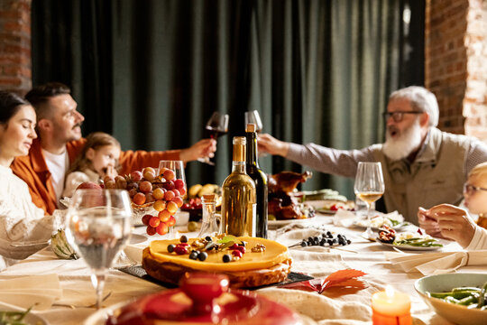 Happy family celebrate Thanksgiving day, sitting at table with roasted turkey and holiday traditional food, dishes. Drinking wine