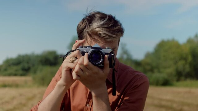 Portrait of professional male photographer shoot stills on film camera in outdoor location. Travel blogger or content creator work in field. Millennial generation z photographer