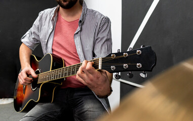 Male musician is playing music on wooden acoustic guitar, capture chords by finger.