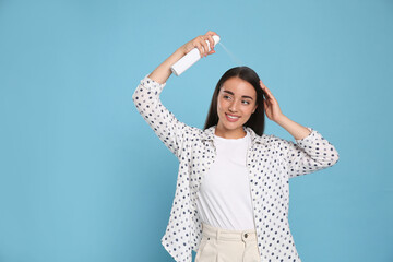 Young woman applying dry shampoo against light blue background