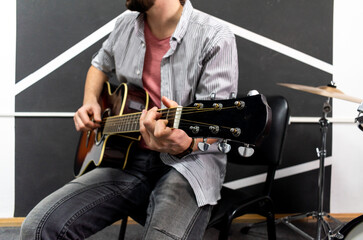 Male musician is playing music on wooden acoustic guitar, capture chords by finger.