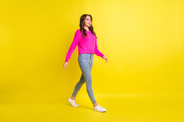 Fototapeta na wymiar Full length photo of shiny pretty curly young lady dressed pink pullover walking looking empty space isolated yellow color background