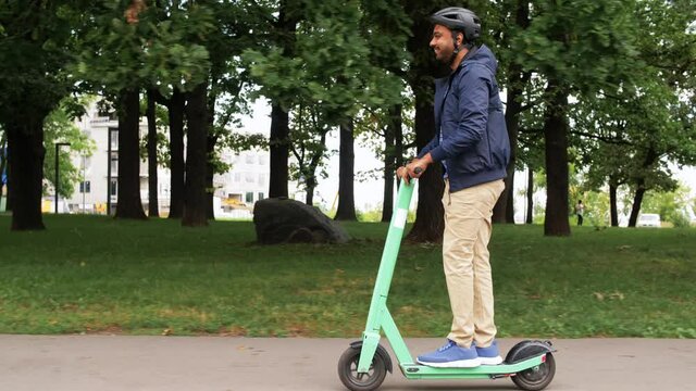 transport, safety and people and concept - happy smiling young man in helmet riding electric scooter on street