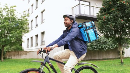 food shipping, profession and people concept - happy smiling indian delivery man in bike helmet with thermal insulated bag riding bicycle on city street