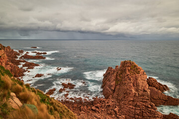 A scenic view overlooking waves breaking against red pillars of rock with the vast ocean on the...