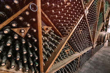 Lots of shelves with old wine bottles covered with dust aging at the vintage wine cellar at the winery.