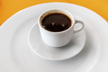 Black hot and fragrant coffee in a mug on a saucer on a bright orange table in the cafeteria