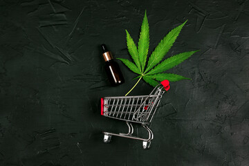 Cannabis oil bottle with marijuana leaf in shopping cart on black background. Online weed store.