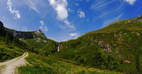 white waterfall in a green mountain landscape with blue sky panorama