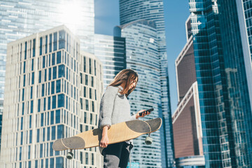 Fototapeta na wymiar Portrait of casually dressed young businesswoman with skateboard using phone near office.