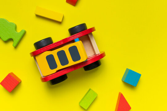 Wooden children's toy red fire truck, Multi-colored children's constructor made of natural wood on yellow background flat lay top view. Kids natural eco toys. Developing toys, game. Special equipment