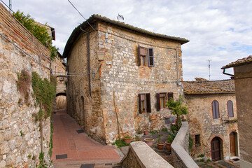 Haus mit Terrasse an einer engen Gasse mit Torbogen in der Altstadt von San Gimignano - obrazy, fototapety, plakaty