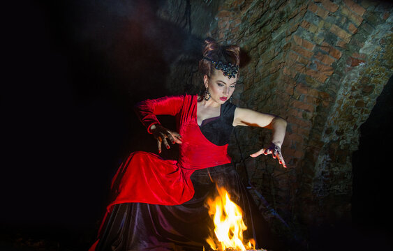 A woman in the image of a witch on Halloween night conjures near the fire.