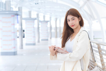 Fototapeta na wymiar Asian working business woman in white suit is outdoors to meet a client at the office her holding hand tablet with a city background.