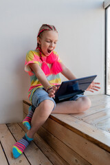 Teenage girl sits on steps near window and records video for blog. Wellness and privacy concept.