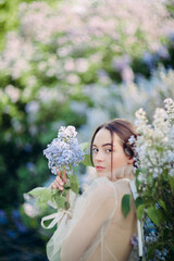 Naklejka premium Portrait of young woman in garden among blooming lilac shrubs.