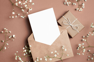 Greeting card mockup, flat lay with gift box, envelope and white gypsophila flowers decorations on paper background.