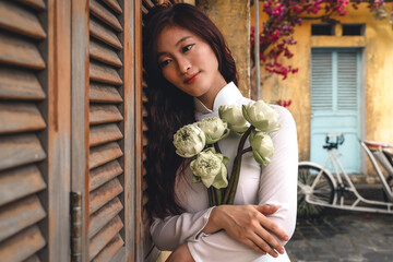 Vietnamese woman in traditional ao dai dress holding flowers