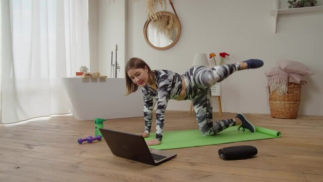 Lovely sporty fit woman watching video tutorial on laptop, performing clamshell exercise, strengthening gluteus medias, improving stability in hips and pelvis while practicing yoga online class