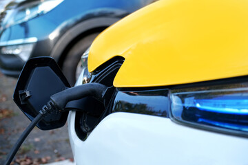 yellow, white passenger electric car replenishes battery at charging station, alternative energy...