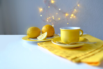 tea still life in yellow, fresh lemons on a plate, a cup of hot aromatic tea, linen napkin, garlands are shining, the concept of tea drinking at home, teatime, warm mood, sweet home