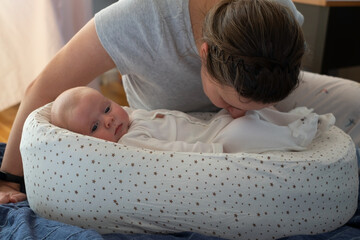Mother sniffing stinky diaper of her little daughter checking if it is time to change it. - obrazy, fototapety, plakaty