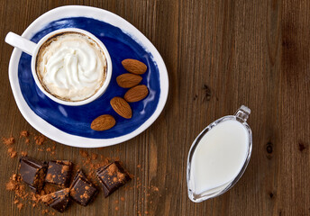 Blue cup of cappuccino, almonds, chocolate and milk in a glass milk jug