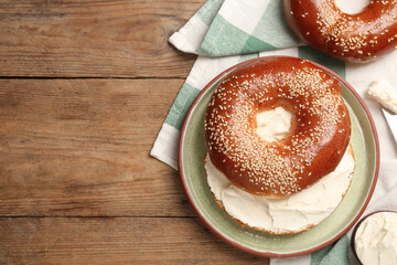 Delicious bagel with cream cheese on wooden table, flat lay. Space for text