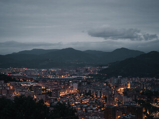 Night photography from a viewpoint; Bilbao illuminated at night. Views of Bizkaia at dusk. Nature, darkness, clouds and mountains in dark Bilbao.