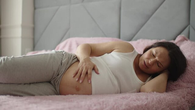 Expectant mother suffering from pregnant pain. Pregnant woman feeling ache lying on a bad.  Pregnant adult woman feels pain  expecting childbirth. Pregnant woman cannot fall asleep from abdominal pain