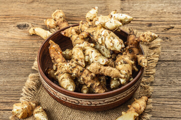 Raw Jerusalem artichoke in a bowl on wooden boards background