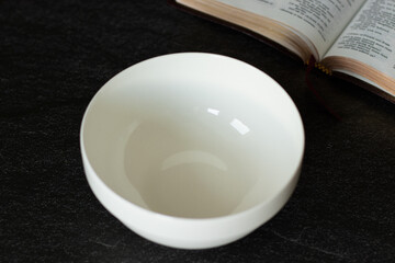 The biblical concept of fasting and repentance. An empty food bowl with an open Holy Bible Book. Atonement Day feast. Repent, fast, have faith, and return to God Jesus Christ. A closeup.