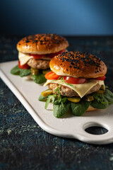 two hamburgers with cutlet on a serving board, blue background, vertical format