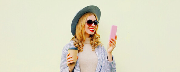 Portrait of smiling young blonde woman with smartphone wearing a hat on background