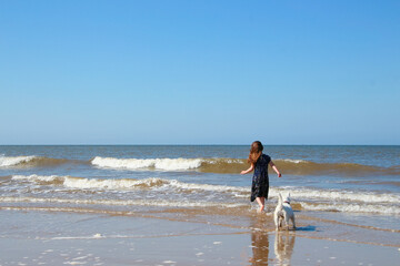 British Summer, UK Holidays vacation in England, young girl playing with a white dog on. Cromer beach in a sunny day of summer, joy, happiness, holiday, Norfolk coast, North sea