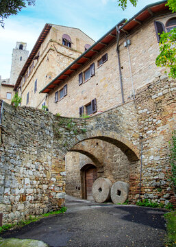 Alte steinerne M&uuml;hlr&auml;der in einer Gasse mit Torb&ouml;gen in der Altstadt von San Gimignano Toskan