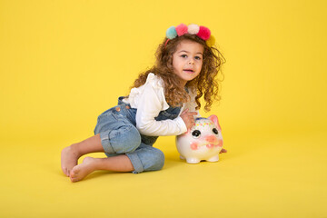 Happy  Little Children girl  saved a little money for future need wearing white T-shirt holding piggy bank, Saving money since childhood on yellow background  studio shot with copy space