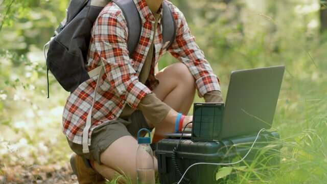 Tilt up shot footage of young Asian woman working on laptop in local forest using portable mini solar panel