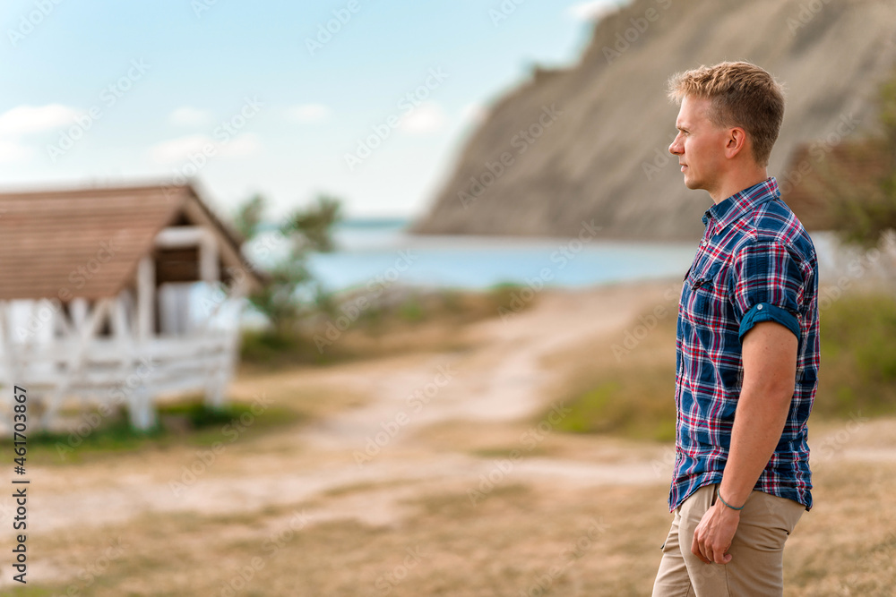 Wall mural A young man in a rustic-style area near a white fence and a view of the mountain on Cape Chameleon, Crimea