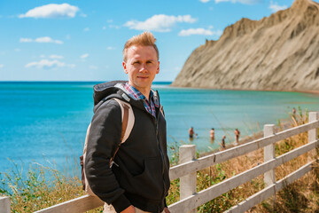 A young man in a rustic-style area near a white fence and a view of the mountain on Cape Chameleon, Crimea