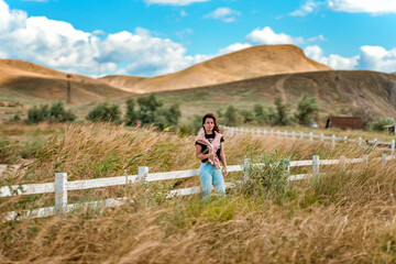 Naklejka premium A charming young woman at a white rustic style fence and a view of hills and mountains