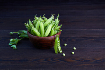 Pods of young green peas in bowl on a dark wooden background.