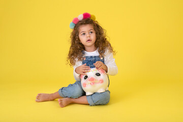 Happy  Little Children girl  saved a little money for future need wearing white T-shirt holding piggy bank, Saving money since childhood on yellow background  studio shot with copy space