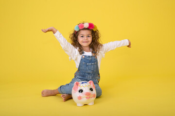 Happy  Little Children girl  saved a little money for future need wearing white T-shirt holding piggy bank, Saving money since childhood on yellow background  studio shot with copy space