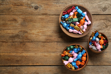 Candies in colorful wrappers on wooden table, flat lay. Space for text