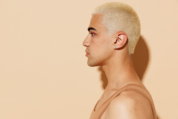 Side view young cool trendy blond stylish twink latin gay man 20s with make up in beige tank shirt...