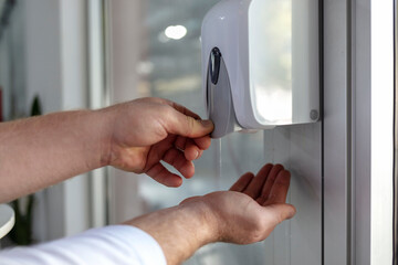 Shot of male hands under automatic alcohol gel dispenser for cleaning hand and clear bacteria for stop Covid 19 virus outbreak. Protection against the virus. Men using alcohol gel for cleaning hands.